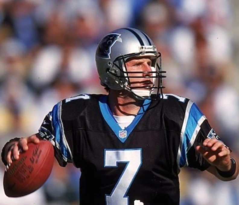 Former NFL Quarterback Steve Beuerlein looking to pass the football while wearing his black and blue Carolina Panthers uniform, number 7.