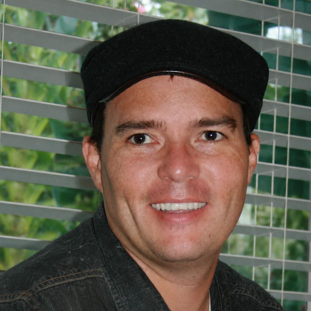 Brandon Gabriel smiling on a golf course wearing a dark patterned polo shirt and a light blue MUNI hat.