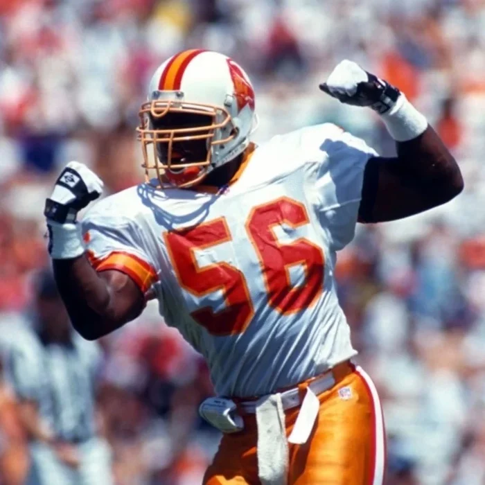 NFL legend Hardy Nickerson Sr. flexing on the field in his classic orange and white Tampa Bay Buccaneers uniform.